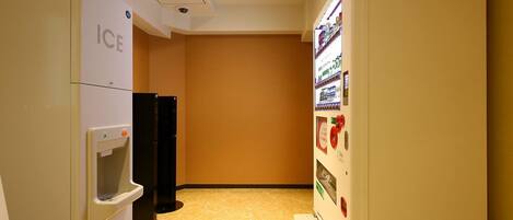 A hallway with an ice dispenser, a refrigerator, and a vending machine.