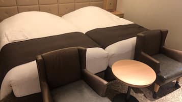 A hotel room with a large bed, two armchairs, a small round table, and a headboard with a light fixture.
