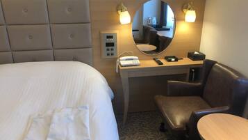 A hotel room with a bed, a desk with a mirror, a chair, and a small table.