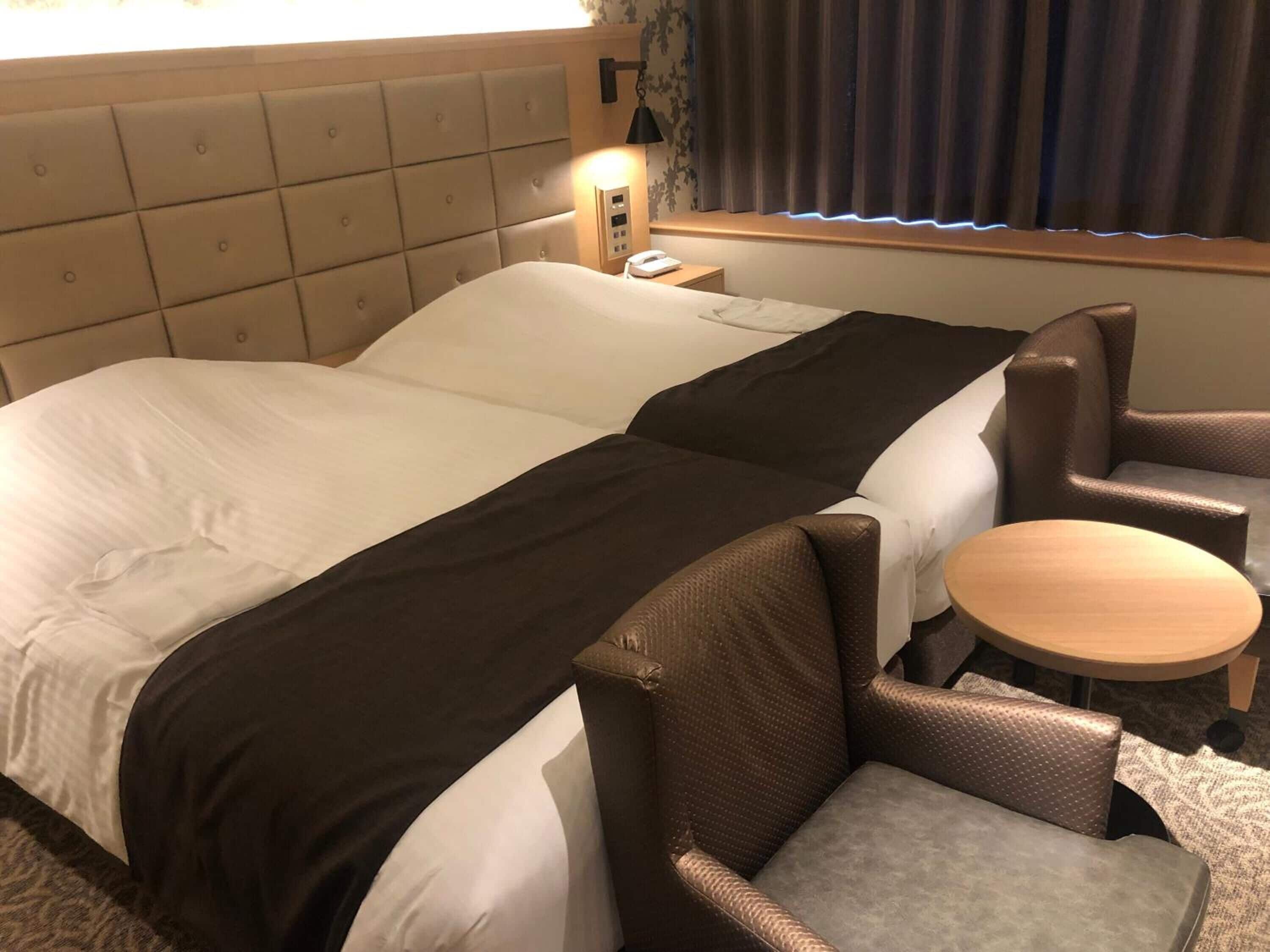 Habitación de hotel con una cama grande, dos sillones, una mesita redonda y una mesita de noche con lámpara.