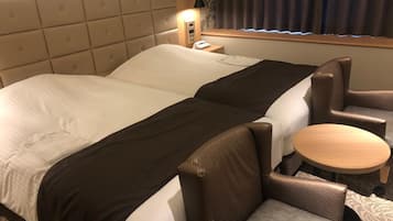 Habitación de hotel con una cama grande, dos sillones, una mesita redonda y una mesita de noche con lámpara.