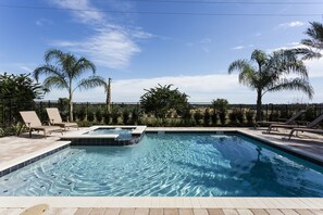 A rectangular swimming pool with a hot tub, surrounded by lounge chairs and palm trees.