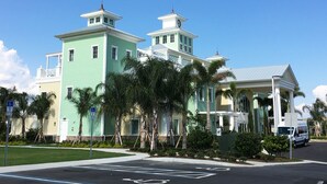 A two-story building with a light green facade, a white balcony, and a small tower with a clock. - Encore Club #1 - 10 Bedroom Private Pool Villa in Reunion Golf Resort (Kissimmee)