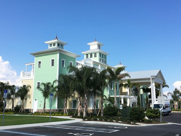A two-story building with a light green facade, a white balcony, and a small tower with a clock.