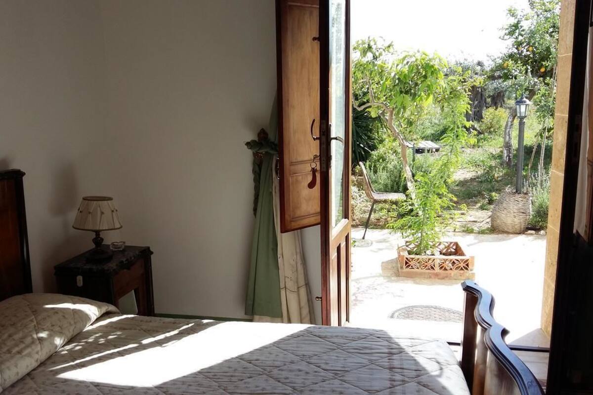 Un dormitorio con cama, mesita de noche, lámpara y vistas a un jardín exterior a través de una puerta abierta.