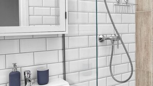A bathroom with white subway tiles, a white sink with two soap dispensers, a glass shower enclosure, and a wooden door. - Elegant Ernesto (Budapest)