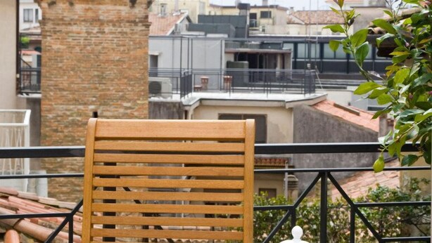 A wooden table set with a teapot, cups, and a fruit bowl on a balcony overlooking a cityscape with a brick tower in the background. - B&B Barberia (Treviso)