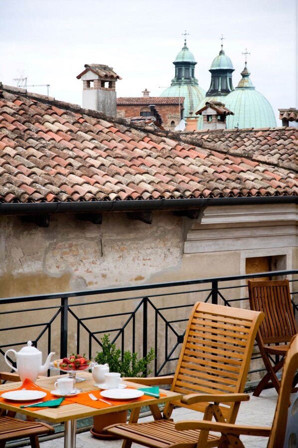 Una terraza con una mesa lista para comer, sillas de madera y una vista de edificios con cúpulas al fondo.