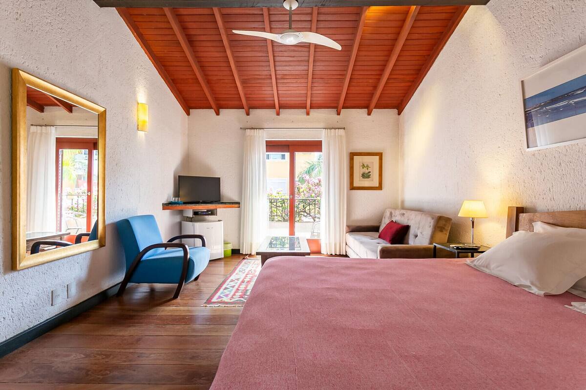 Ein Hotelzimmer mit Bett, einer Sitzecke, einem Fernseher, einem Sessel und einem Balkon mit Blick.