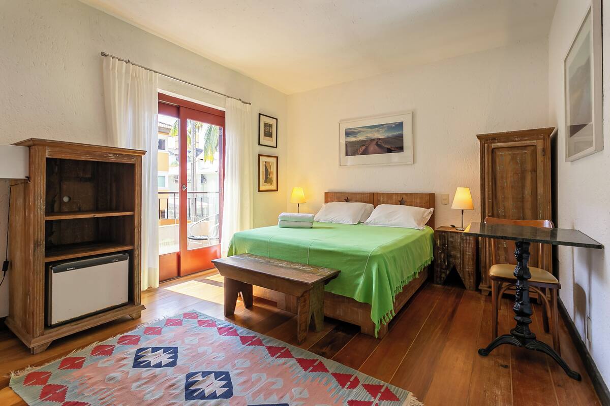 Ein Schlafzimmer mit Bett, Nachttisch, Lampe, Holzschrank, Bank und einem gemusterten Teppich.