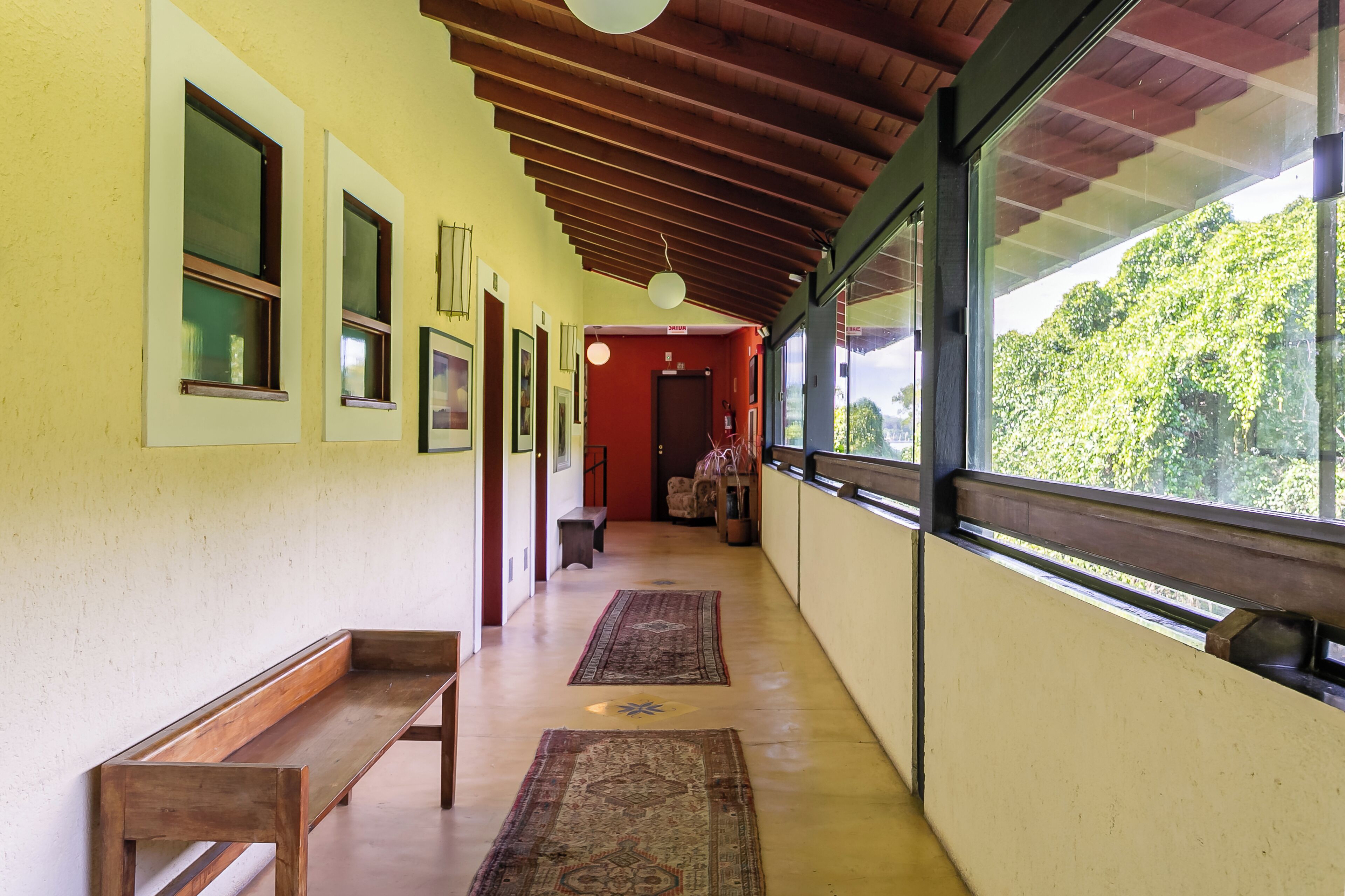 A corridor with benches, patterned rugs, and large windows offering a view of greenery.