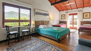 A room with a bed, two bedside tables, a desk with chairs, and a window with a view of greenery. - Pousada Casa da Lagoa (Florianópolis)