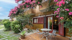 A wooden deck with a table and chairs, surrounded by lush greenery and flowering plants. - Pousada Casa da Lagoa (Florianópolis)