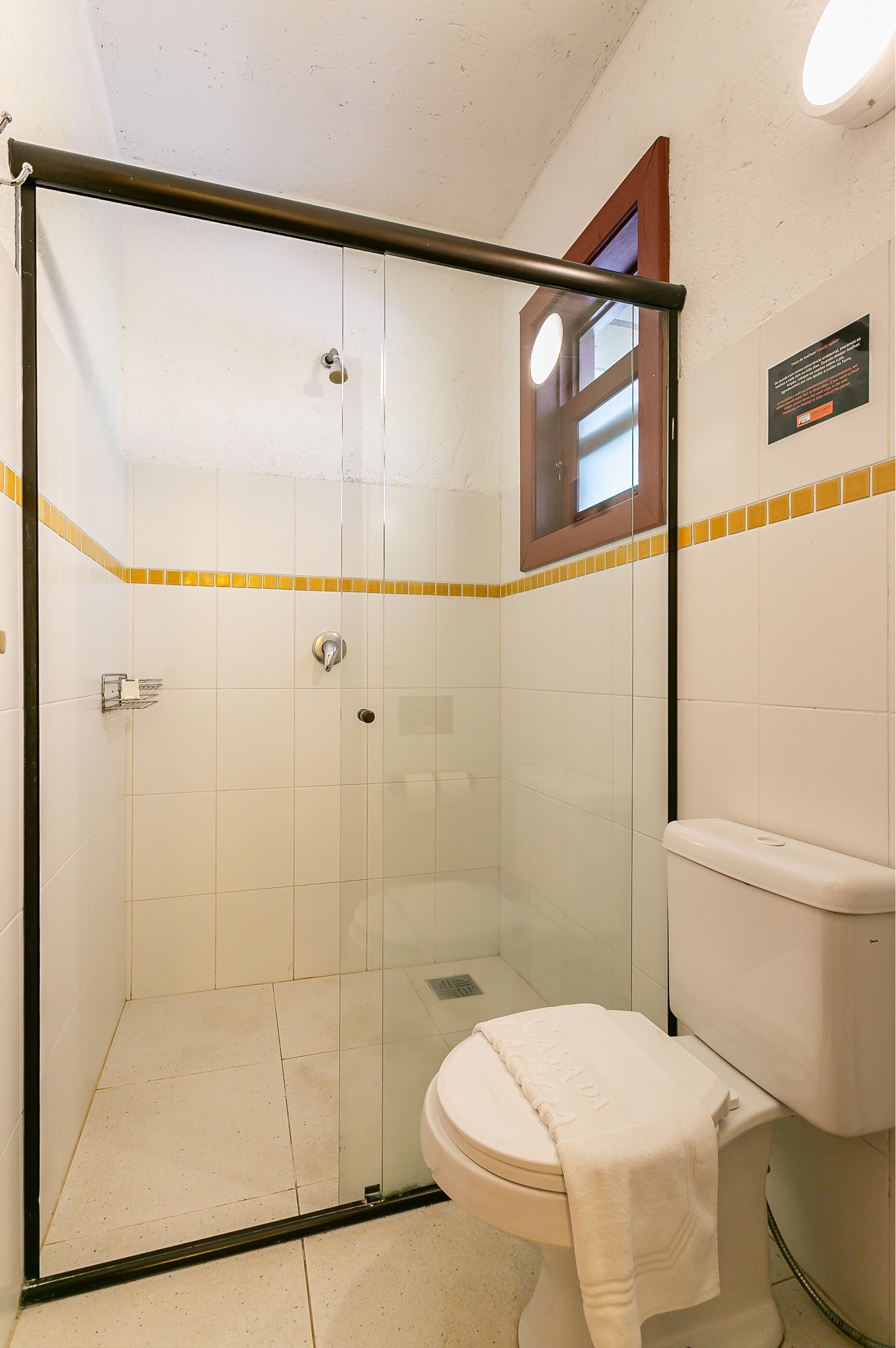 A bathroom with a glass-enclosed shower, a toilet, and a small window.