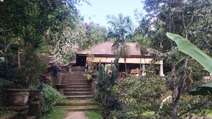A house with a red tiled roof, surrounded by lush greenery and a stone staircase leading to the entrance. - Puri Sangkih (Munduk)