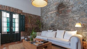 Una sala de estar acogedora con una pared de piedra, un sofá blanco, una mesa de centro de madera y una lámpara colgante.