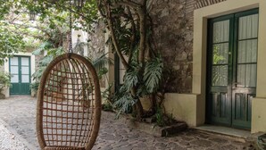 Un patio empedrado con una silla de mimbre, un muro de piedra y una puerta con una contraventana verde.