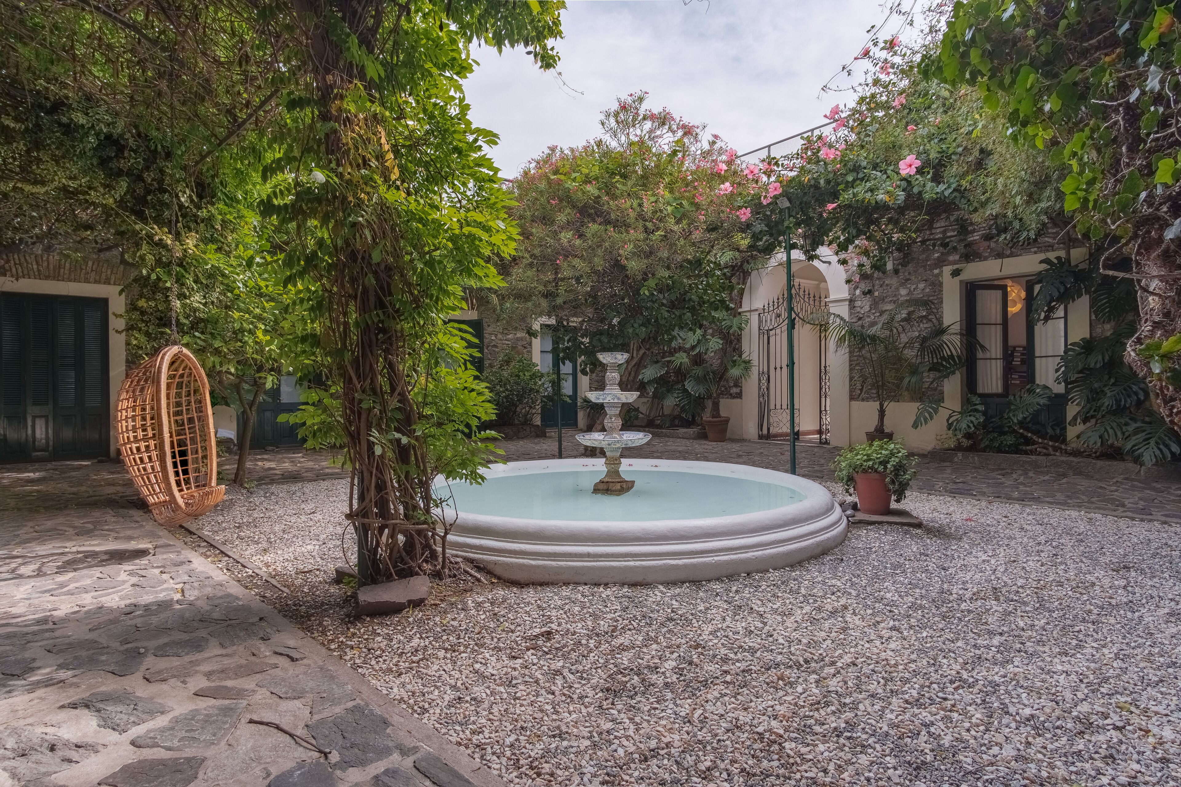 A courtyard with a circular fountain, a wicker swing, and various potted plants.