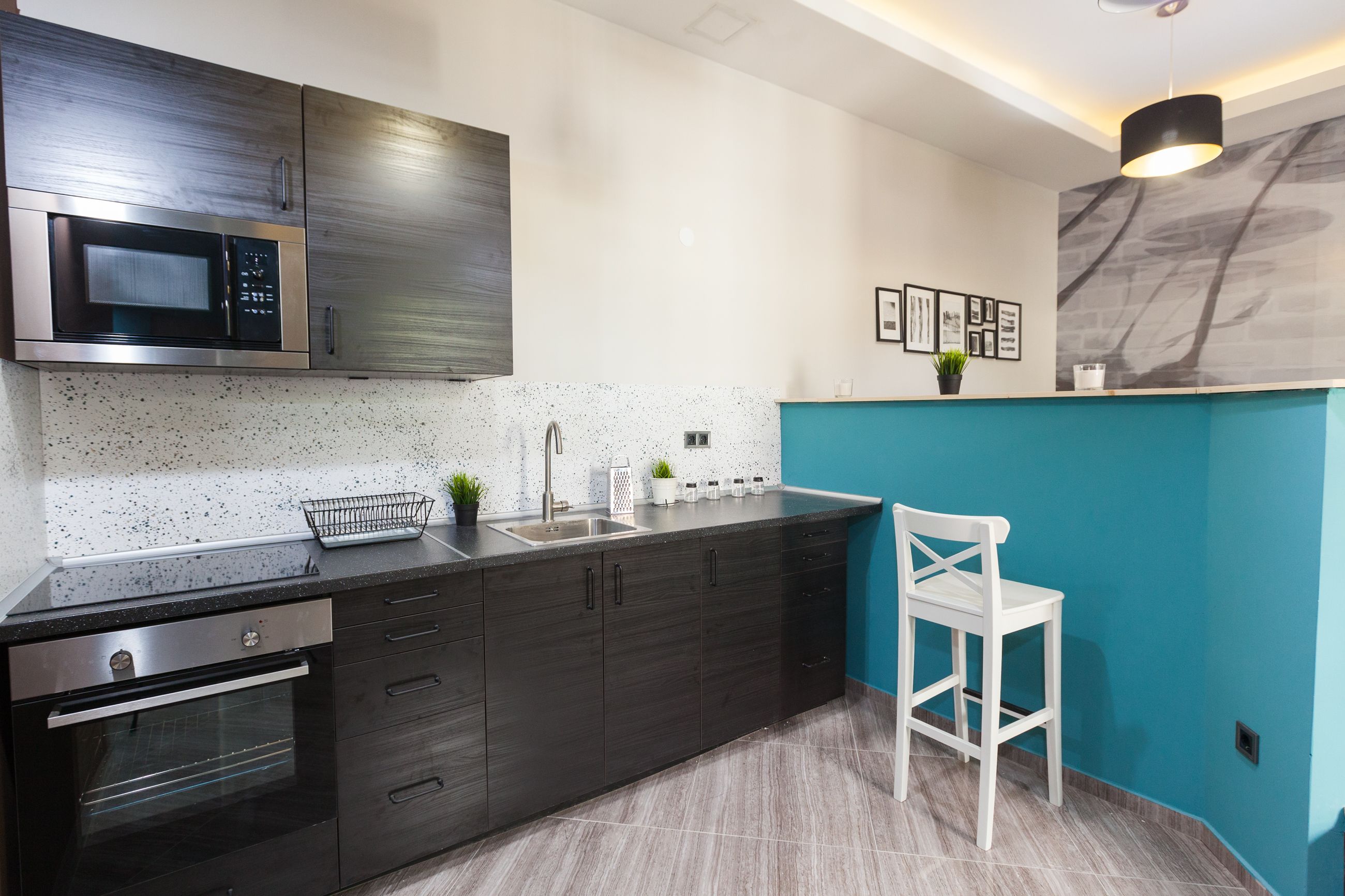 A modern kitchen with dark cabinetry, a stainless steel microwave, a built-in oven, a sink, and a teal accent wall.