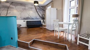 A modern living room with a wooden floor, a black sofa, a white dining table with chairs, and a large window with curtains. - Fancy Ernesto II (Budapest)