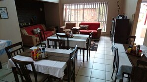 A dining area with multiple tables and chairs, a sofa, and a television. - Gold Reef Place (Johannesburg South)
