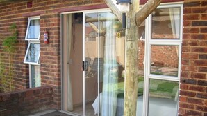 A brick building with a sliding glass door entrance, a fire extinguisher mounted on the wall, and a doormat with "GOLD REEF GUEST HOUSE" written on it. - Gold Reef Place (Johannesburg South)