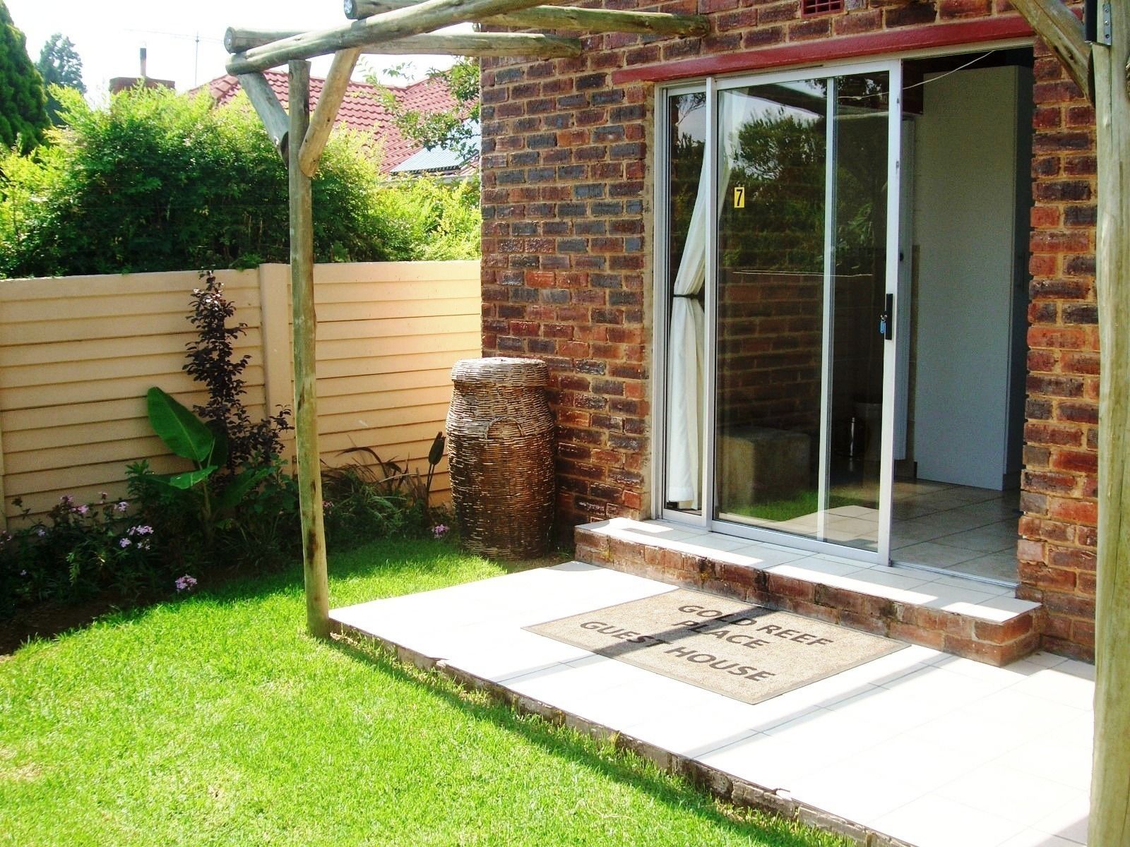 A brick house with a sliding glass door, a wooden pergola, and a doormat reading "Gold Reef Guest House".