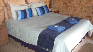 A bed with a light blue bedspread and pillows, a dark blue throw blanket, and a blue towel. - Gold Reef Place (Johannesburg South)
