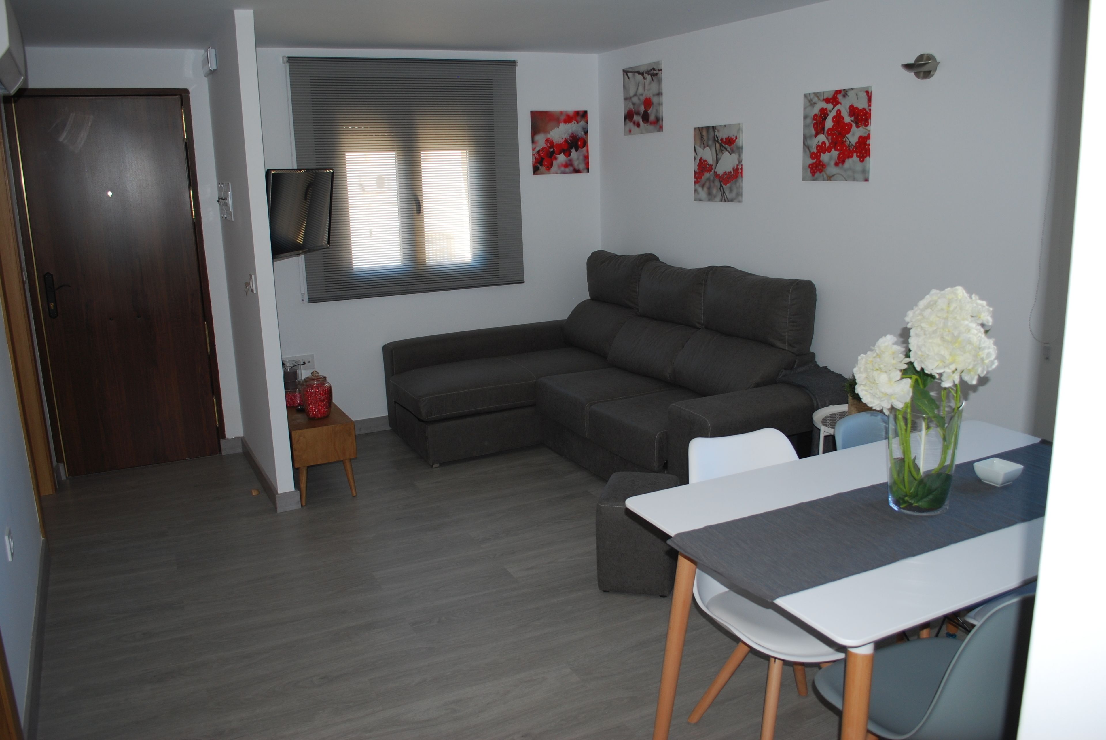 A modern living room with a sectional sofa, a dining table with chairs, and a vase of flowers.