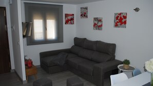 A modern living room with a sectional sofa, a small side table, and a round table with a plant. - Apartamentos Rurales El Trillo (Malpartida de Plasencia)