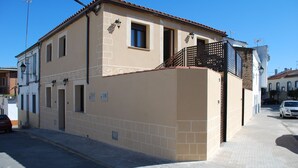 A two-story building with a beige facade, a small balcony with a black railing, and a visible door. - Apartamentos Rurales El Trillo (Malpartida de Plasencia)