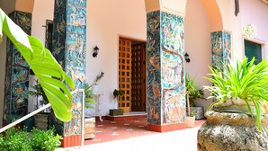 Une cour avec un sol carrelé, une porte en bois et des colonnes ornées de peintures murales colorées.