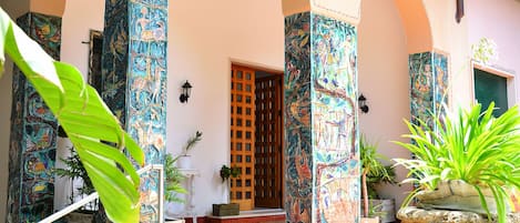 A courtyard with tiled flooring, a wooden door, and columns with colorful murals.