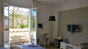 Une chambre d’hôtel comprenant un lit, un bureau, une chaise, une télévision et un balcon avec vue sur la verdure.