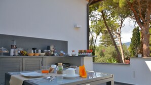Une cuisine extérieure moderne, dotée d’une table à manger, d’appareils de cuisine et offrant une vue sur les arbres et les montagnes.