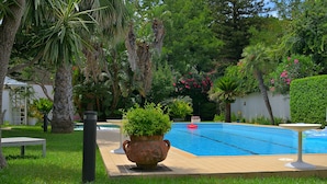 Une piscine entourée d’une végétation luxuriante et agrémentée d’un belvédère blanc.