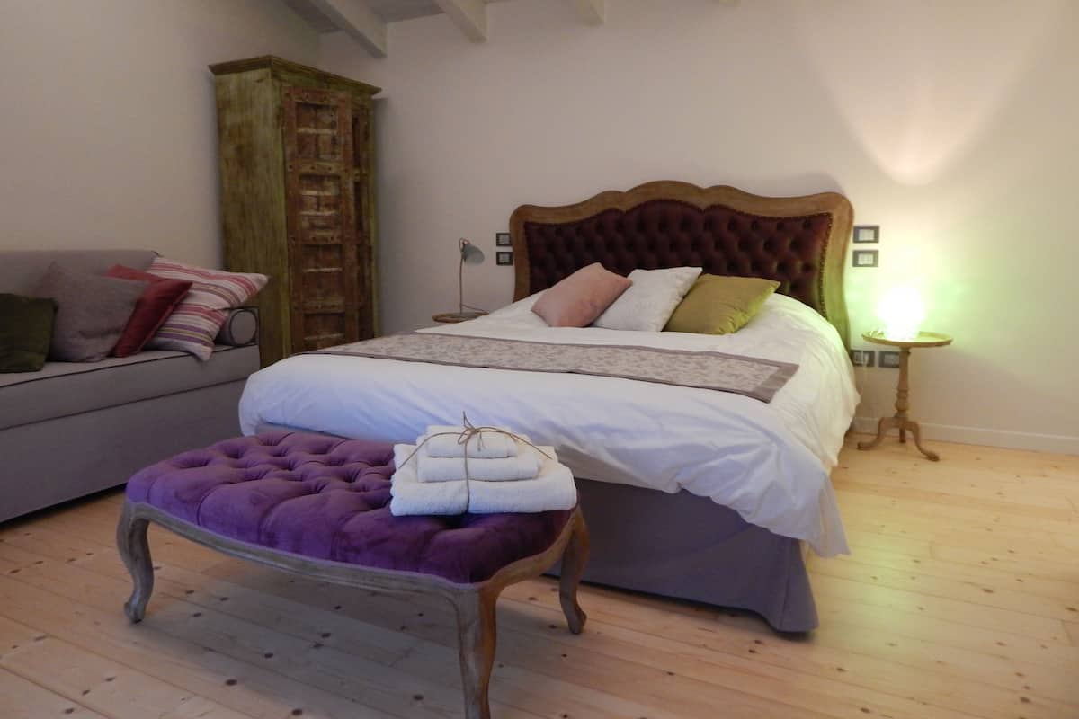 Een slaapkamer met een bed, een houten garderobe, een paars gestoffeerde bank en een nachtkastje met een lamp.