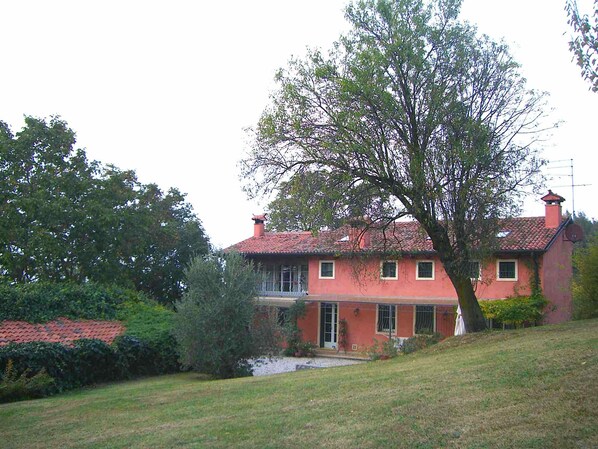 A two-story house with a red roof, surrounded by greenery and a small pond.