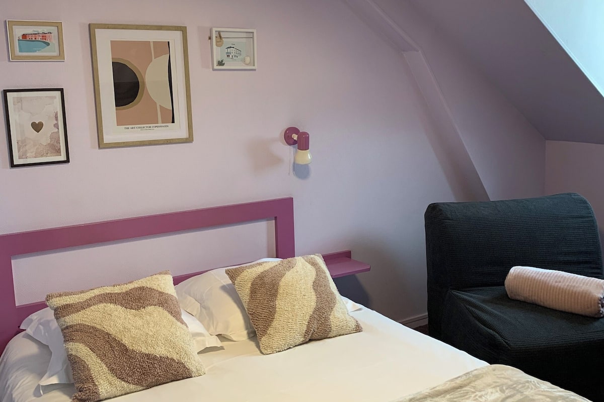 A bedroom with a bed, a chair, and artwork on the wall.