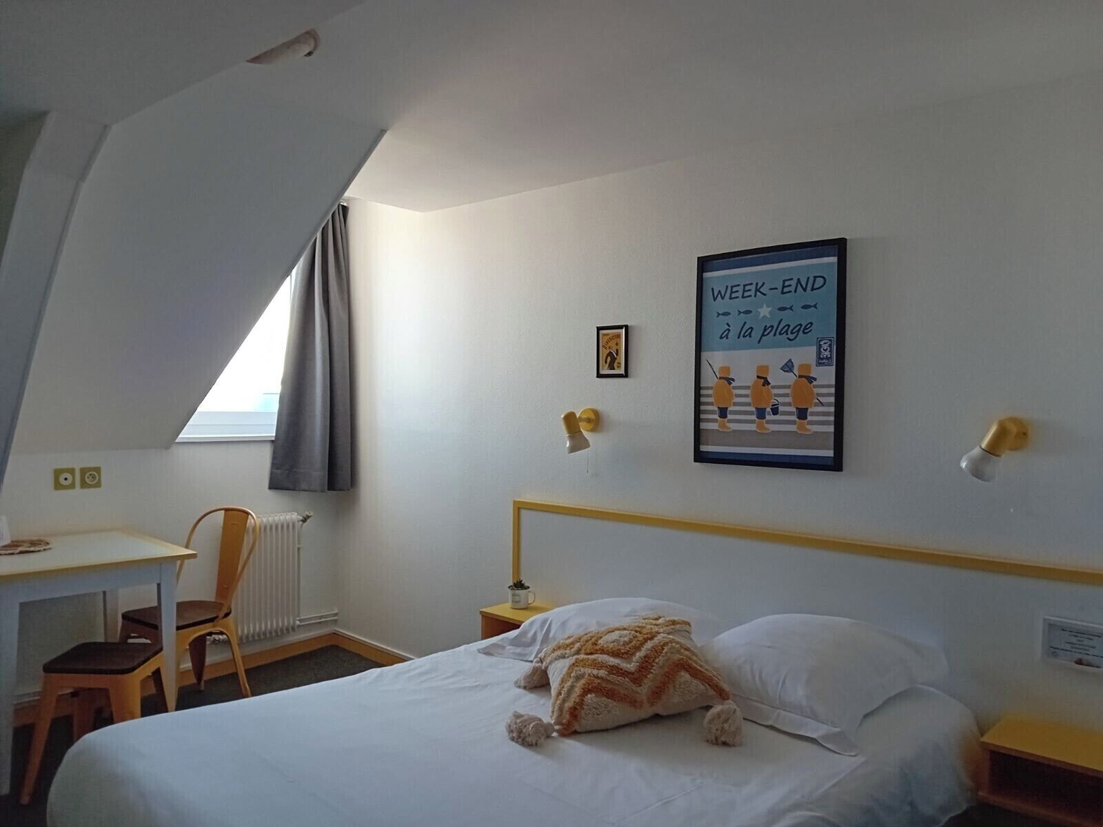 Een hotelkamer met een bed, een bureau, een stoel, een radiator en een poster aan de muur.