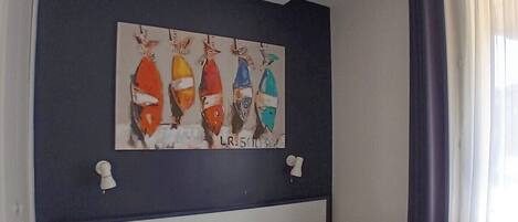A hotel room with a bed, a nightstand, a wall-mounted painting of fish, and a window with curtains.