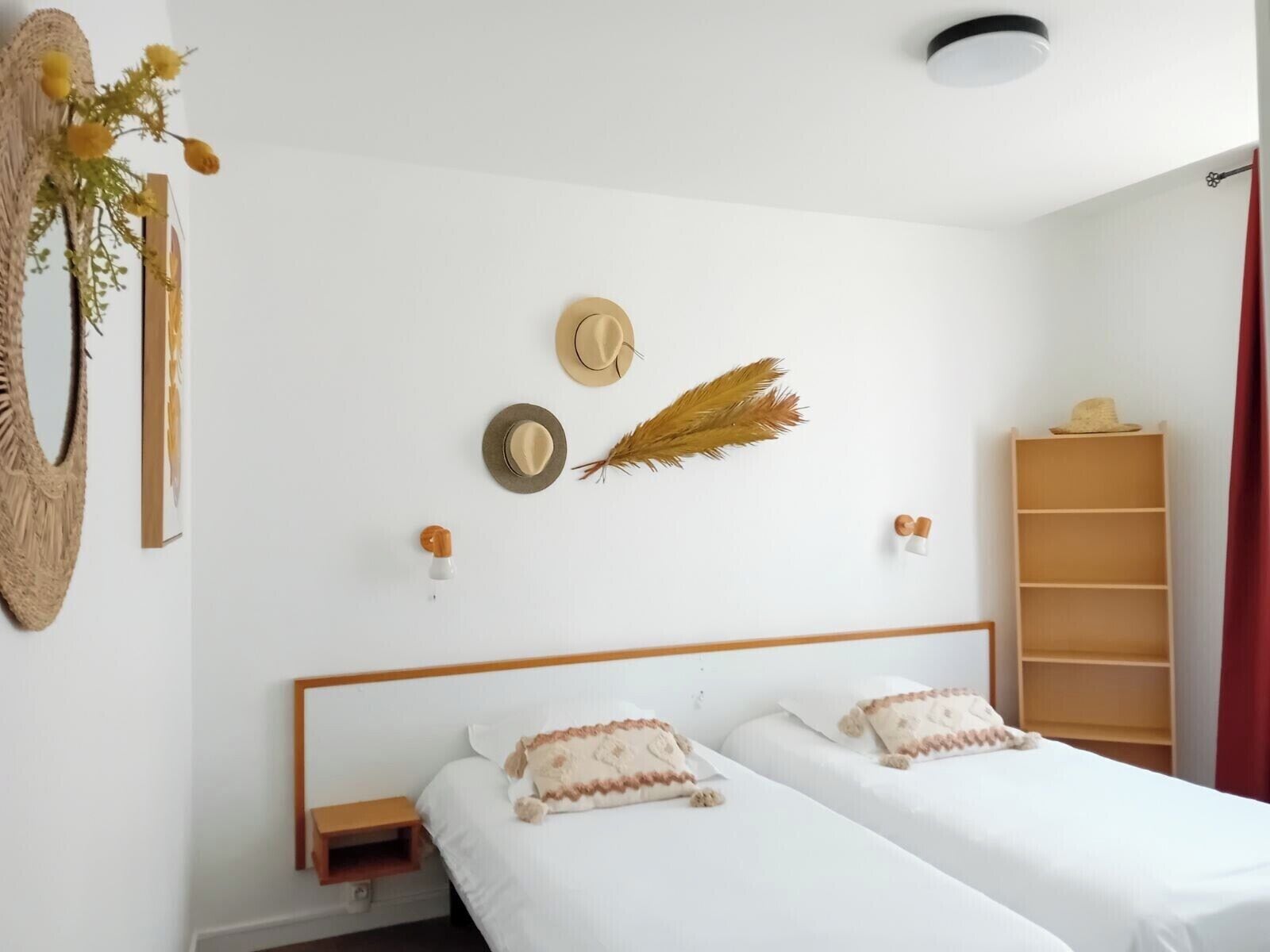 A room with two beds, a wooden headboard, a shelf with hats, and a wall-mounted decorative item.