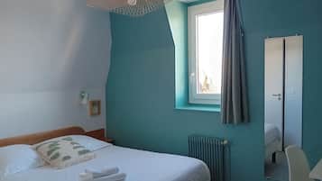 Un dormitorio con cama, ventana con cortinas, radiador, espejo y lámpara colgante.