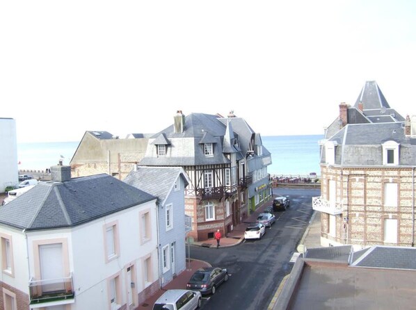 A coastal street with buildings, including a Tudor-style house and a brick structure, leading to the sea. - Hôtel de la Plage (Fecamp)