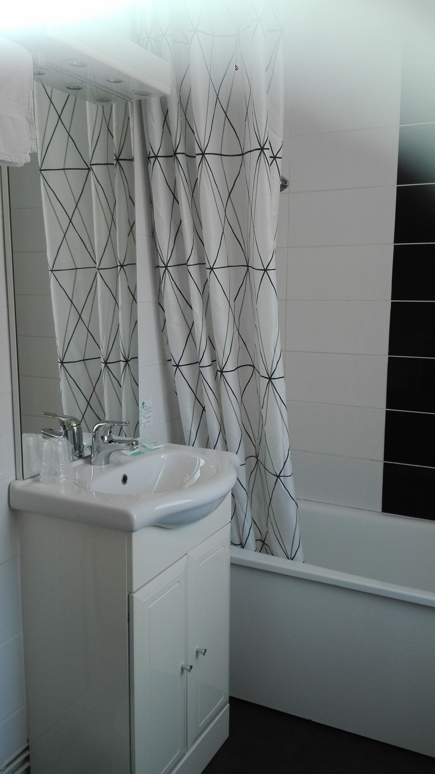 Un baño con lavamanos blanco, espejo y cortina de ducha con estampado geométrico.