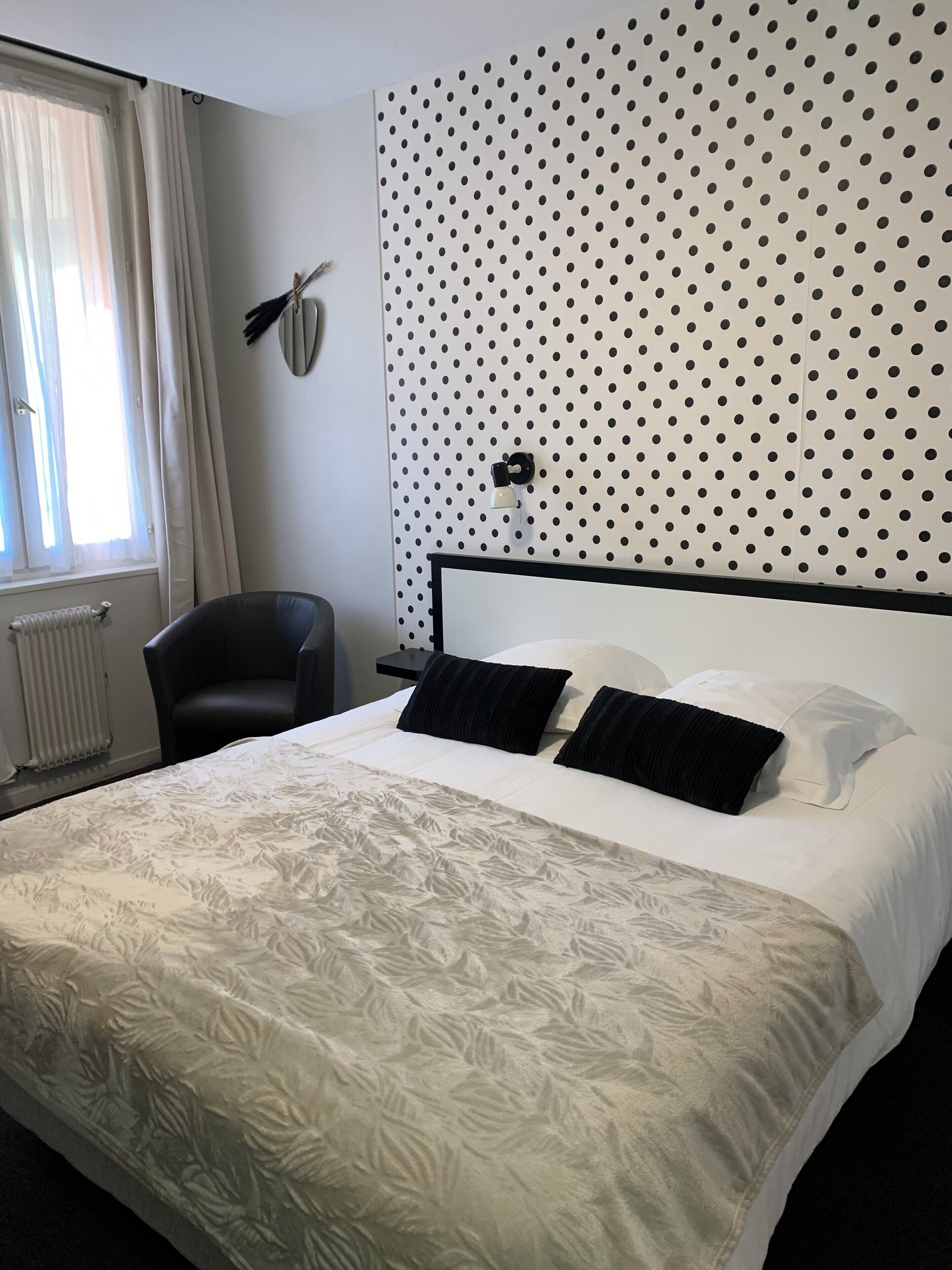 A hotel room with a bed, a chair, a radiator, and a polka dot wall.