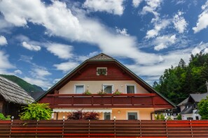 Un chalet traditionnel doté d’un toit à pente, d’un balcon en bois et offrant une vue sur la forêt environnante.