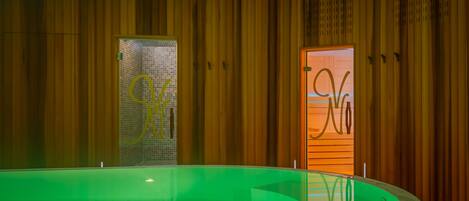 A spa area with a green heated pool, wooden panel walls, and a glass door with a logo.