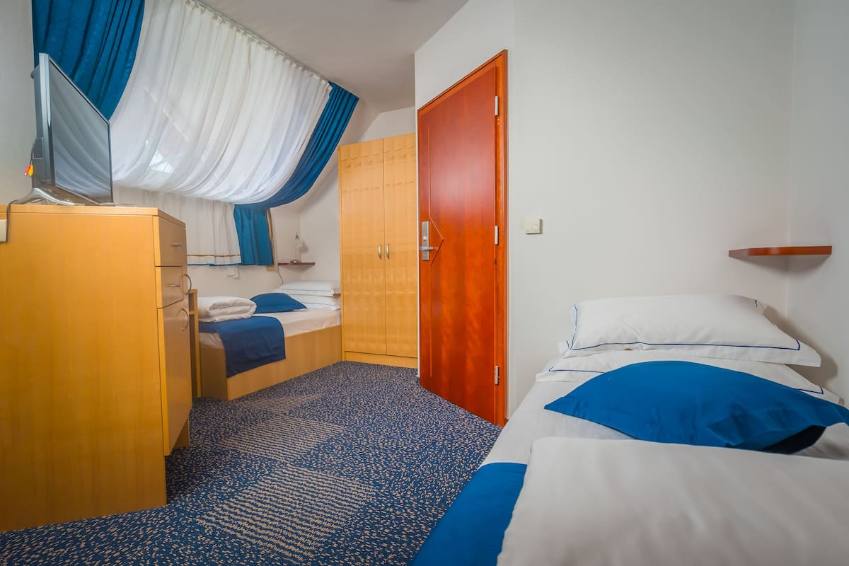A compact hotel room with a bed, a wooden wardrobe, a desk with a chair, and a small bedside table.