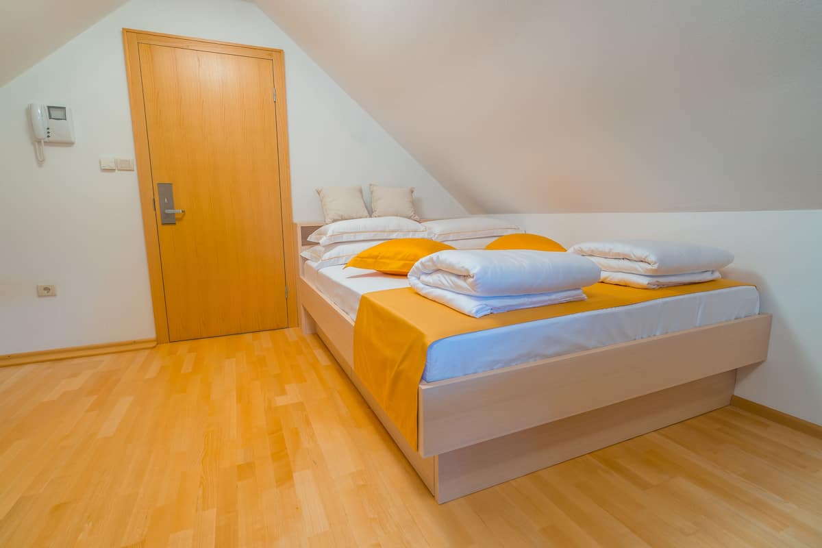 A bedroom with a wooden door, a bed with white and orange bedding, and a light-colored headboard.